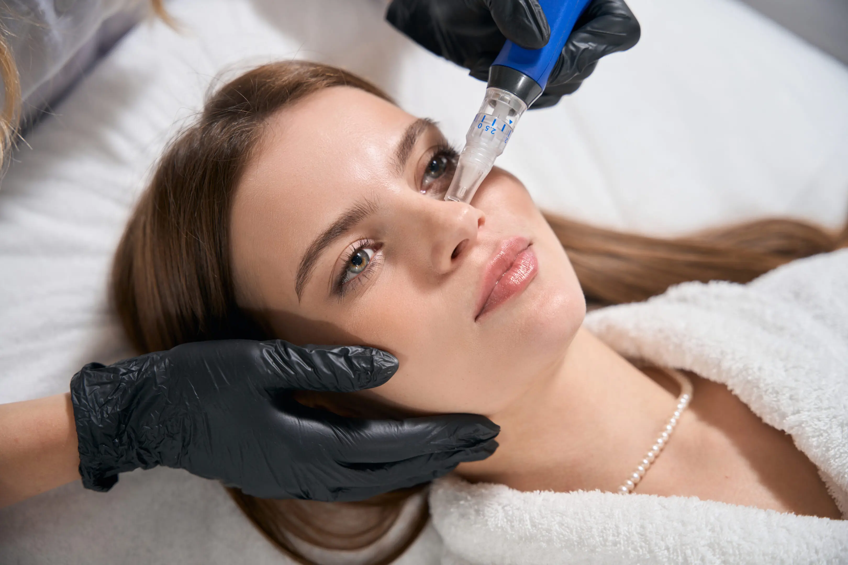 Partial female beautician doing ultrasonic cleaning of face skin with skinpen with micro needle of young caucasian woman in beauty salon. Concept of face skin care and rejuvenation